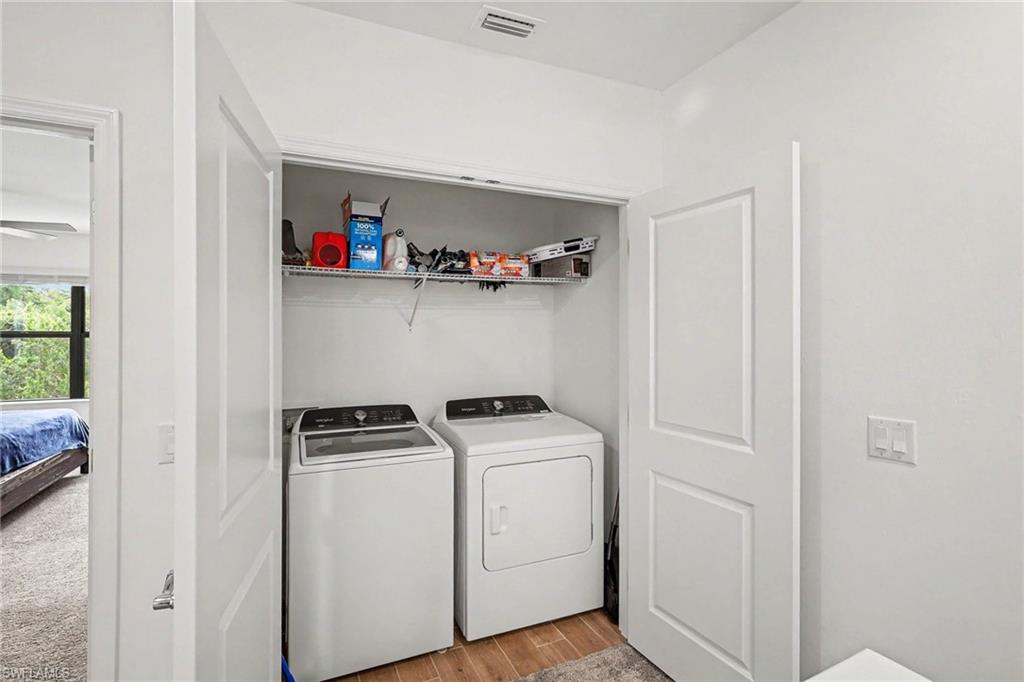 Laundry closet featuring a top-load washer and front-load dryer, wire shelving, and wood-finish flooring