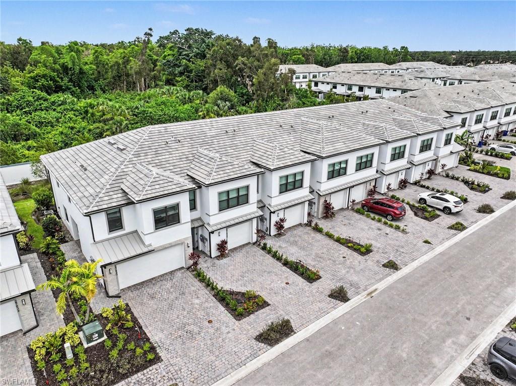 Modern townhome row featuring white exteriors with gray trim, individual attached garages, paver driveways, and landscaped front entries