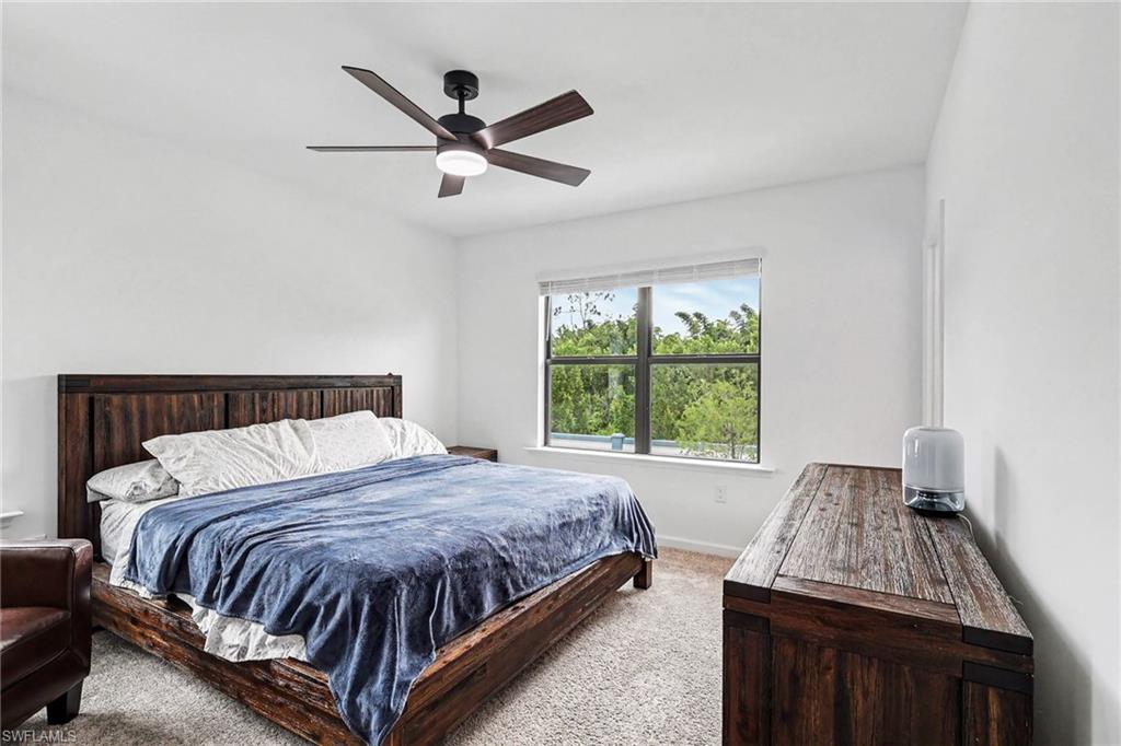 Bedroom featuring a large window, a ceiling fan with integrated lighting, textured carpeting, and white wall finishes