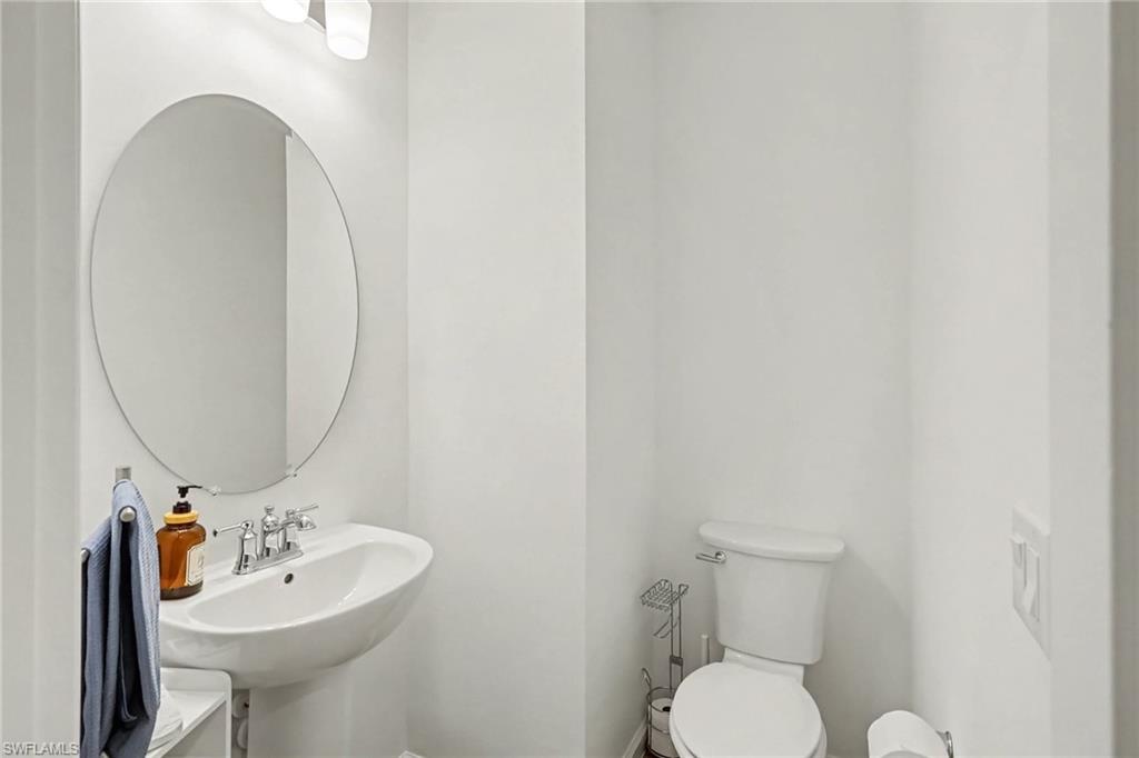 Pedestal sink with chrome faucet, oval mirror, and wall-mounted vanity lighting