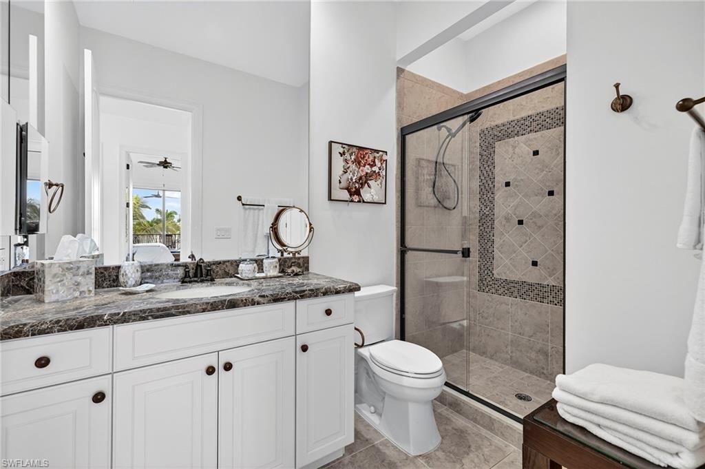 Ensuite bathroom featuring vanity, a stall shower, ceiling fan, and light tile patterned floors