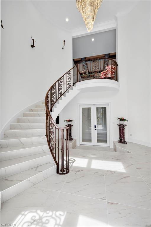 Staircase with french doors, a chandelier, marble finish flooring, recessed lighting, and ornamental molding