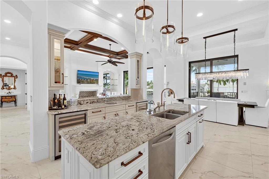 Kitchen featuring arched walkways, light stone counters, an island with sink, a ceiling fan, and decorative light fixtures