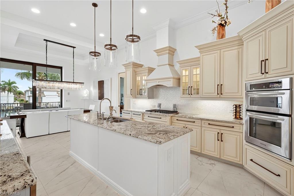 Kitchen with cream cabinetry, decorative light fixtures, double oven, ornamental molding, and recessed lighting