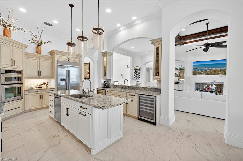 Kitchen with cream cabinetry, arched walkways, light stone counters, ceiling fan, and ornamental molding