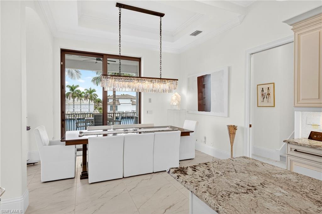 Kitchen featuring light marble finish floors, light stone counters, decorative light fixtures, ornamental molding, and a raised ceiling
