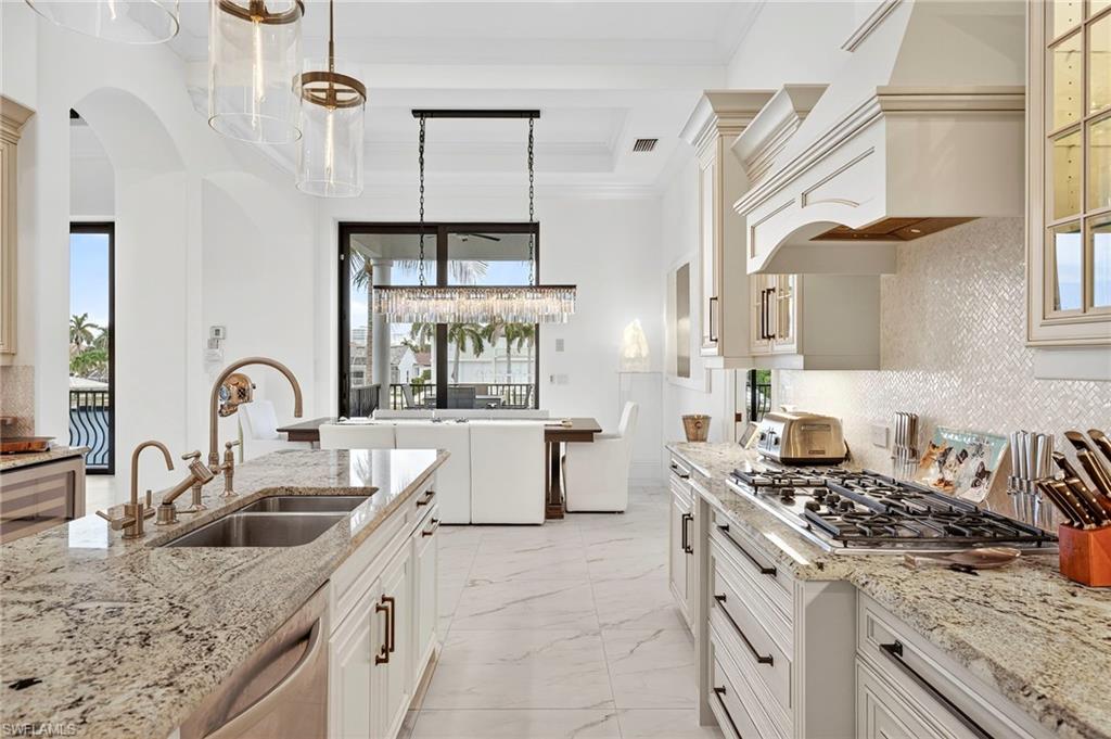 Kitchen with backsplash, pendant lighting, light stone countertops, light marble finish floors, and appliances with stainless steel finishes