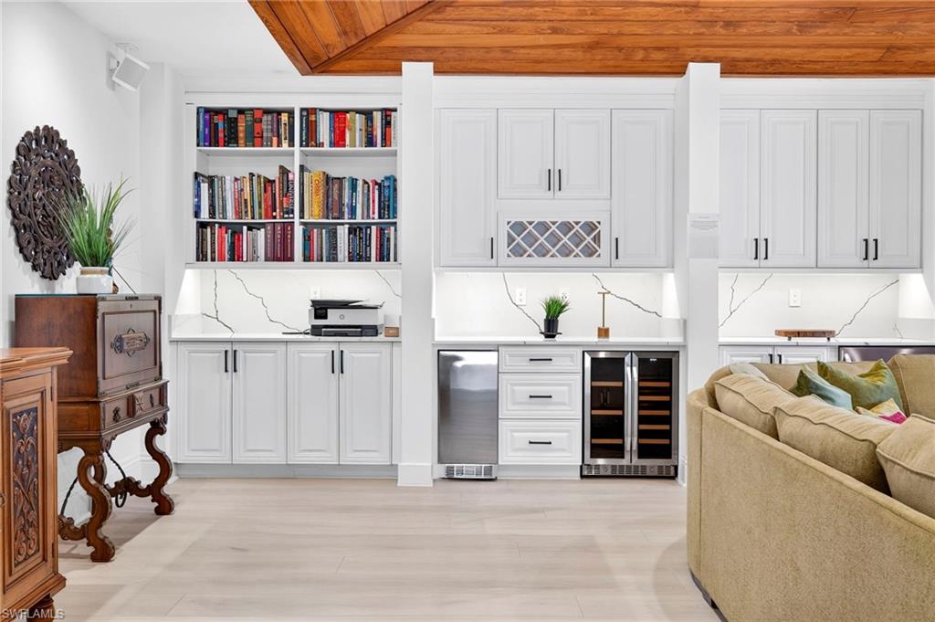 Indoor bar with white cabinets, wine cooler, open shelves, stainless steel refrigerator, and wood ceiling