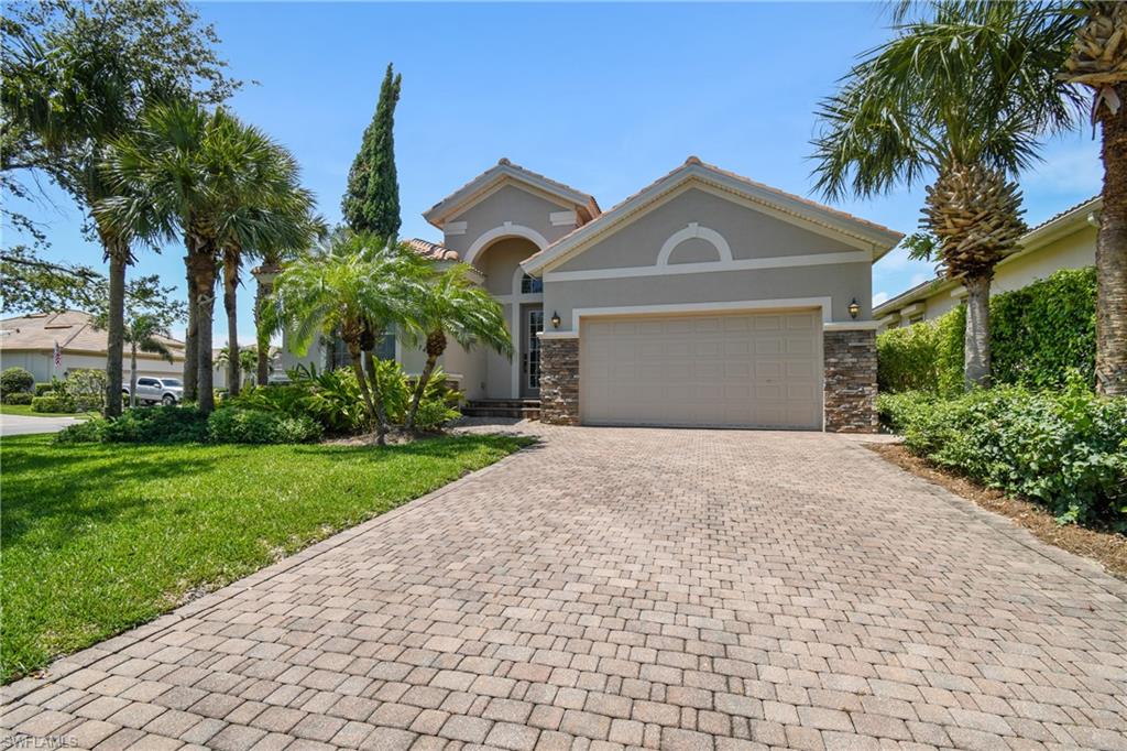 Exterior featuring a paver driveway, stone accents, stucco facade, arched entryway, and tropical landscaping