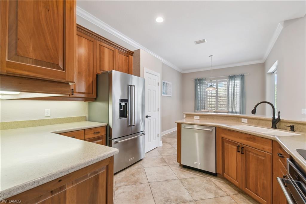 Modern kitchen featuring recessed lighting, extensive wood cabinetry, light-toned countertops, a stainless steel French door refrigerator, and tile flooring