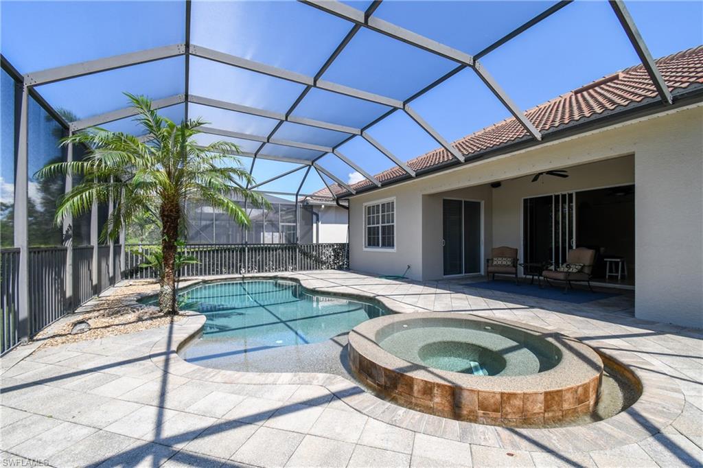 Screened lanai featuring a freeform swimming pool, integrated spa with tile surround, and paver decking