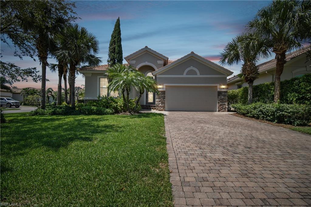 Contemporary stucco exterior with a stone accent facade, a paver driveway, an attached garage, and mature palm trees