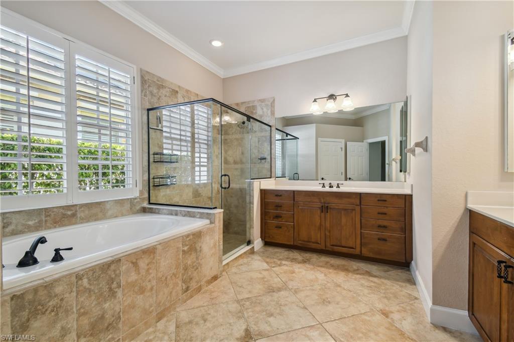 Expansive bath featuring a large soaking tub, separate glass-enclosed shower, custom wood cabinetry, and plantation shutters