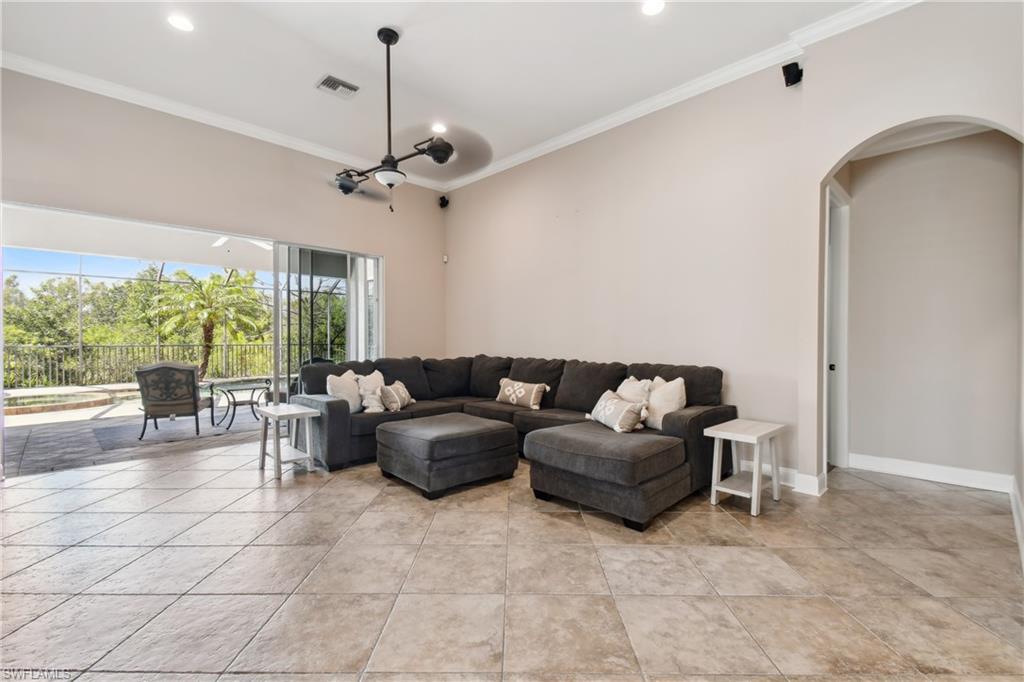 Spacious living area featuring large format floor tiles, crown molding, an arched doorway, and a ceiling fan with integrated lighting