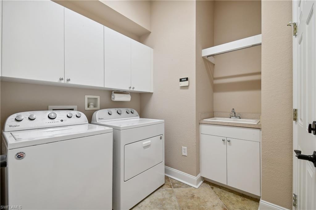 Utility room with upper white cabinetry, a built-in sink with lower storage, and neutral-toned floor tiling