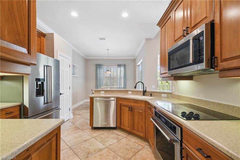 Kitchen featuring wood cabinetry, stainless steel appliances, speckled countertops, and tile flooring