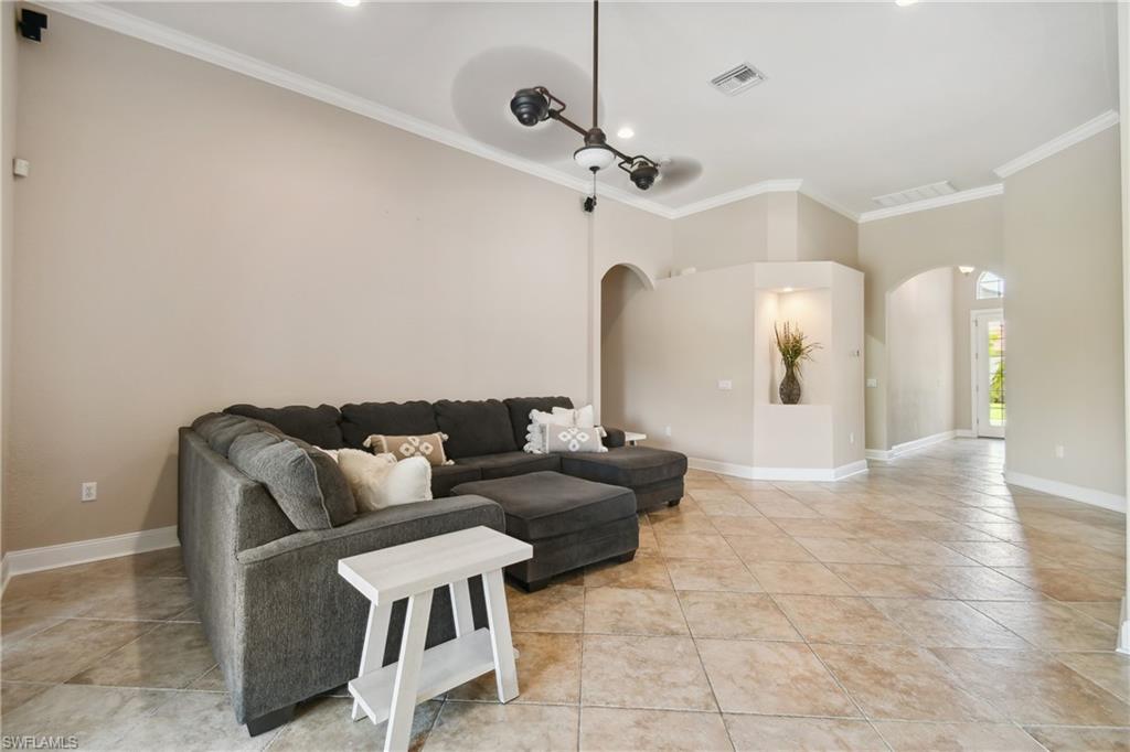 Spacious living area featuring large format diagonal tile flooring, crown molding, arched doorways, a built-in display niche with accent lighting, and a modern ceiling fixture