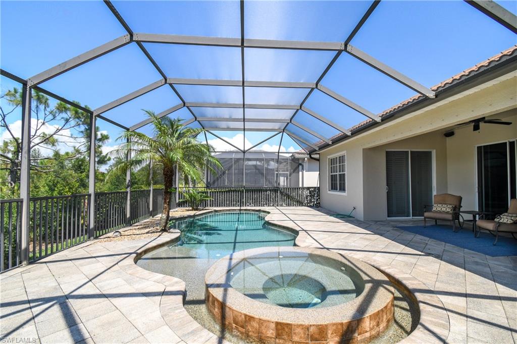 Screen-enclosed outdoor living area featuring a freeform pool, integrated spa with stone surround, and an expansive paver patio