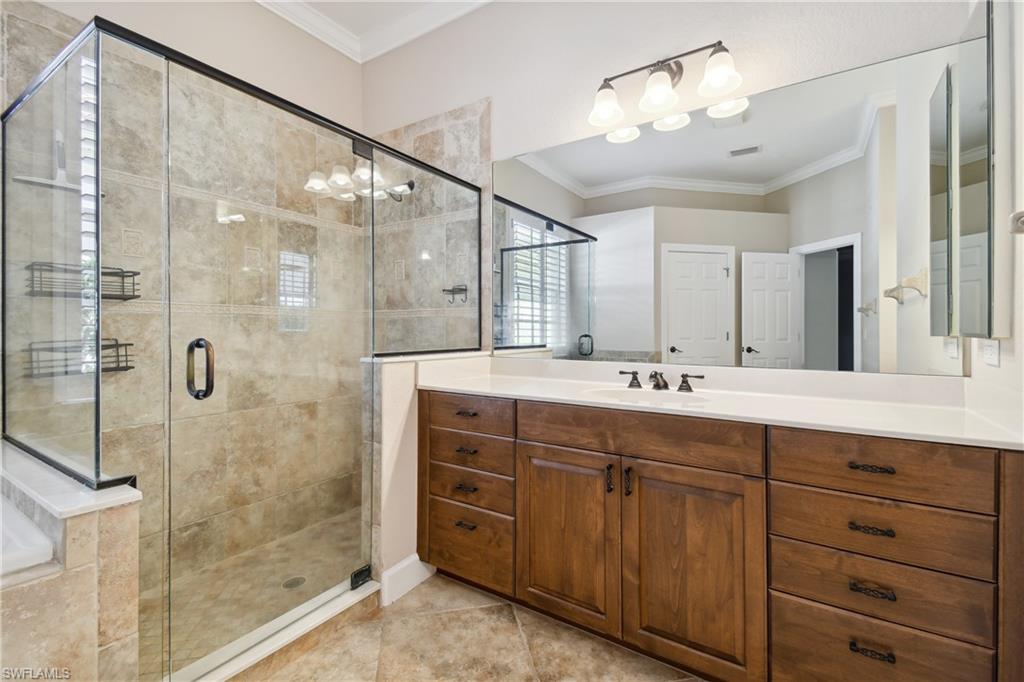 Walk-in glass shower enclosure with tile surround, wood-finish vanity with countertop, undermount sink, and wall-mounted mirror