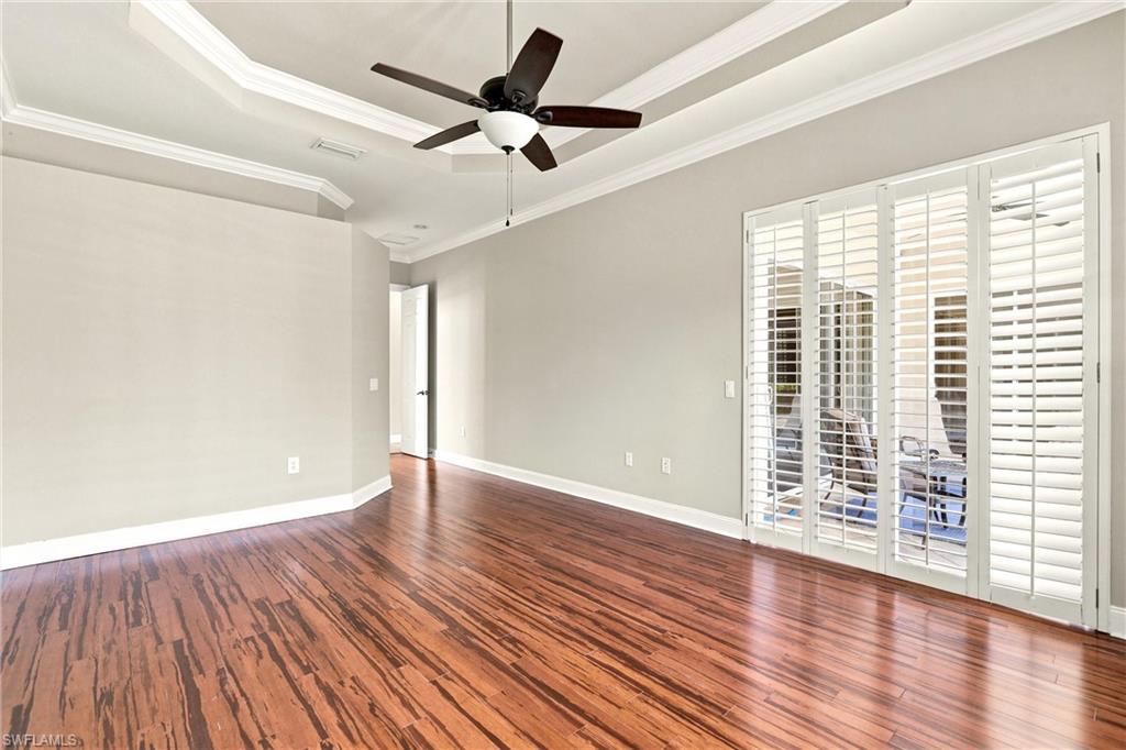 Spacious room featuring wood-finish flooring tile and a tray ceiling with a dark-toned ceiling fan