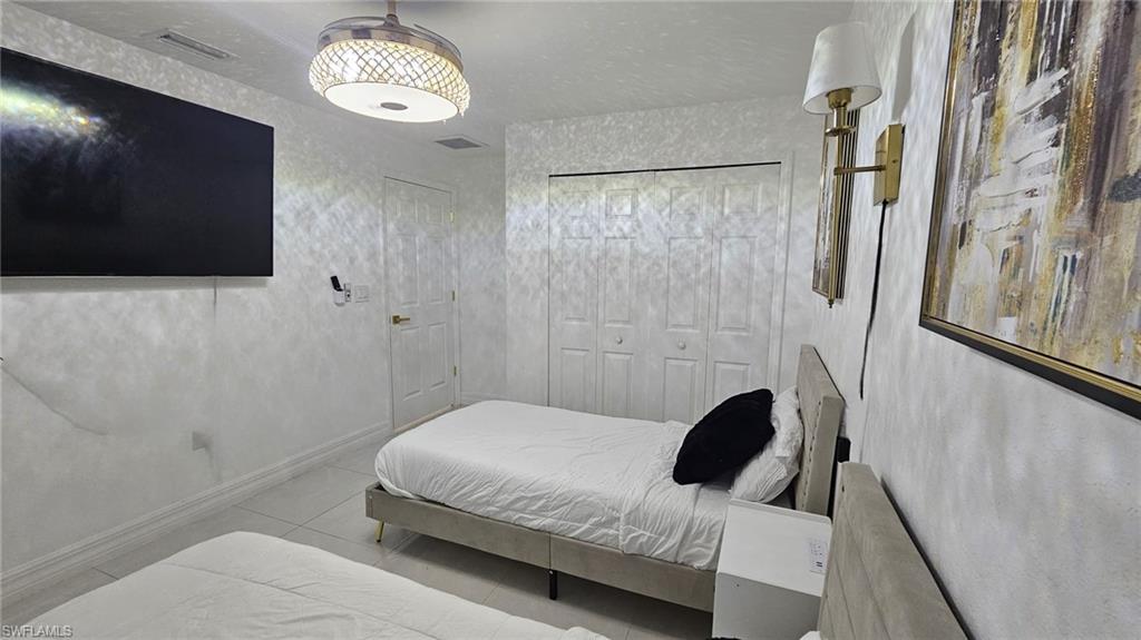 Room featuring light-colored tile flooring, white textured walls, and a ceiling fan with an ornate light fixture