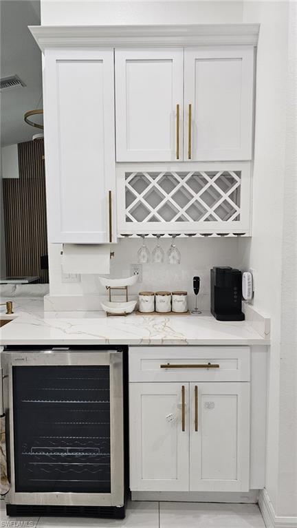 Built-in beverage station featuring white shaker-style cabinetry, a wine rack, integrated stemware storage, a quartz countertop with subtle veining, and a stainless steel beverage cooler