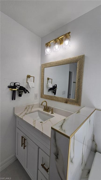 Bathroom vanity featuring a single undermount sink, a stone-finish countertop with veining, gold-tone hardware, and a matching gold-tone framed mirror