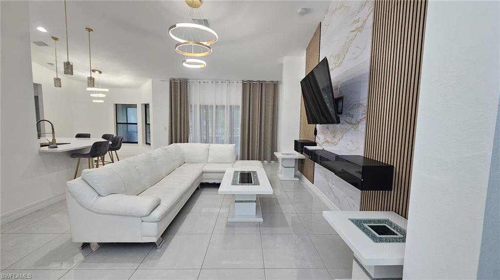 Open concept living area featuring large format tile flooring, a statement accent wall with vertical slat wood panels and a stone-look finish, multiple contemporary light fixtures, and a kitchen island with a waterfall countertop