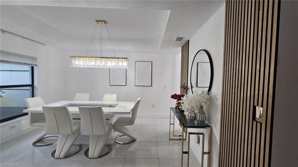 Spacious dining area featuring a linear crystal chandelier, tray ceiling, and large window with blinds