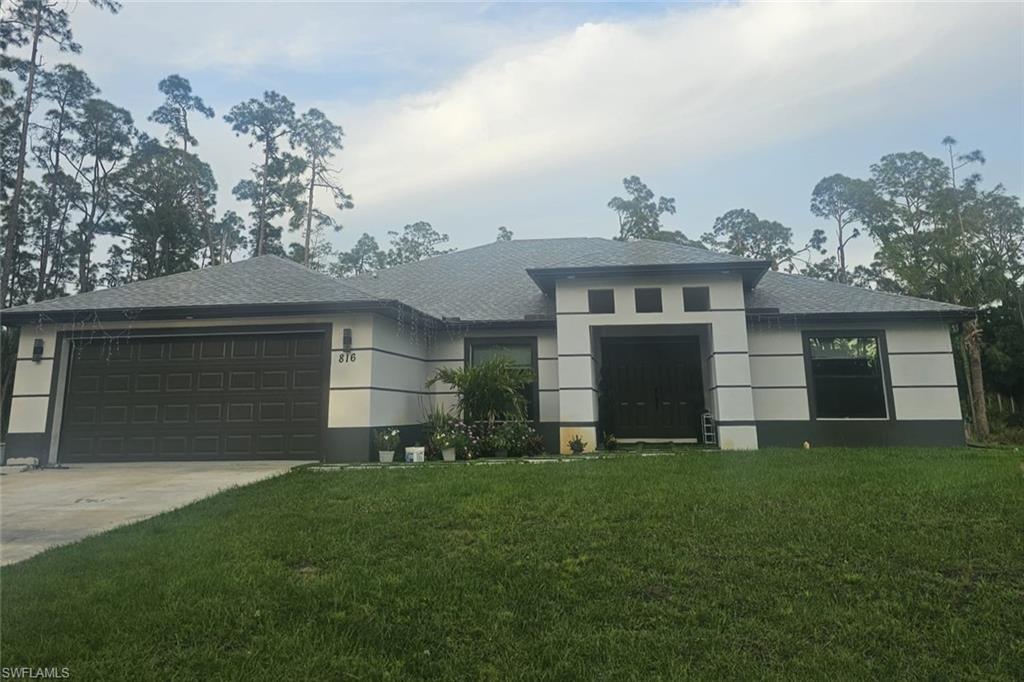 Modern stucco exterior with contrasting trim, a dark paneled garage door, a covered entry, and a gravel shingle roof