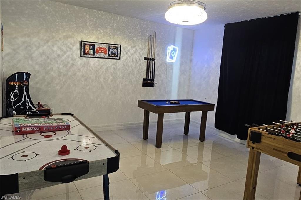 Spacious entertainment area featuring light-toned tile flooring, textured wall finishes, and a flush-mount ceiling fixture