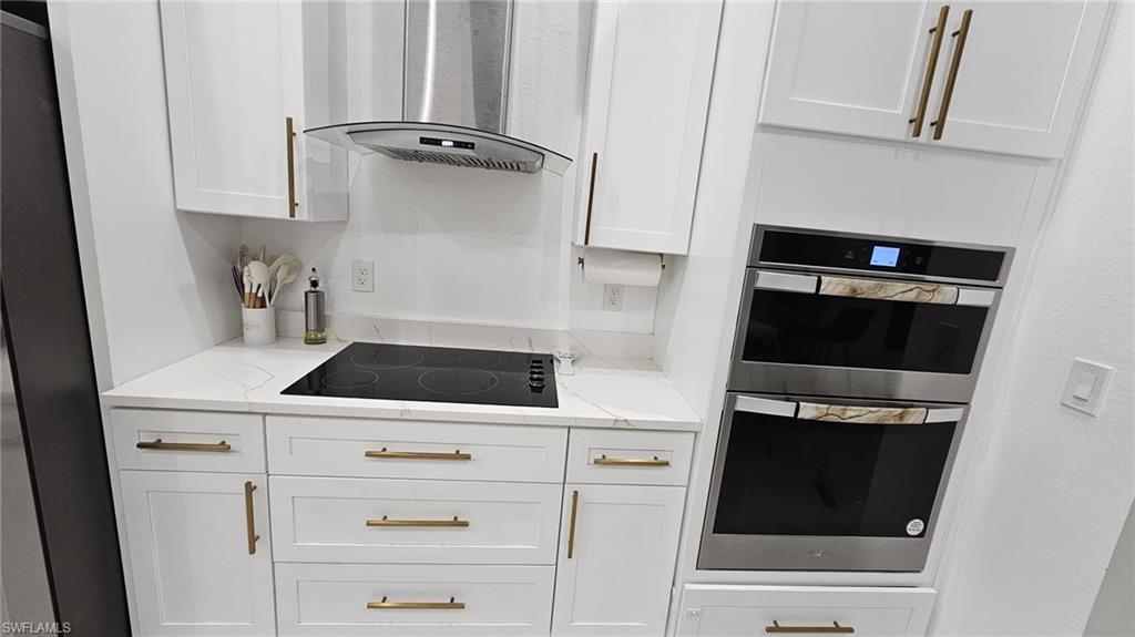 Modern kitchen featuring white cabinetry with brass-finish hardware, a built-in double oven, and a sleek cooktop