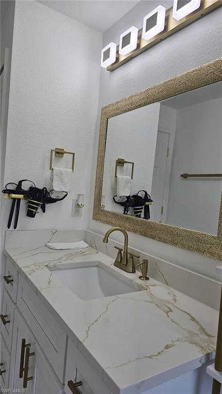 Vanity featuring white cabinetry with gold-tone hardware, a rectangular undermount sink, and a white countertop with gold veining