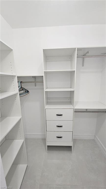 Walk-in closet featuring built-in white shelving, three white drawers with contemporary hardware, and light-toned tile flooring