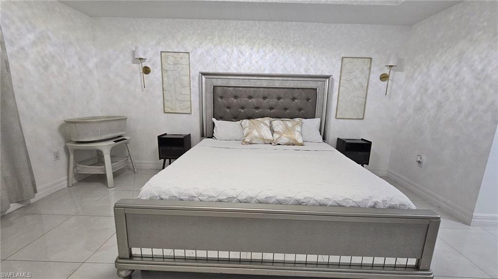 Spacious room featuring large format tile flooring, contemporary wall sconces, textured wall finish, and a substantial bed frame with an upholstered headboard