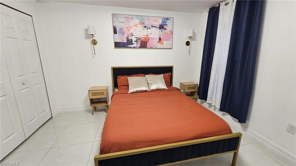Bedroom featuring bi-fold closet doors, white tile flooring, and wall-mounted sconces