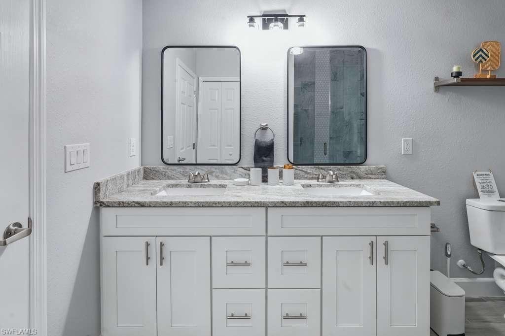Bathroom featuring double vanity, a textured wall, and a stall shower