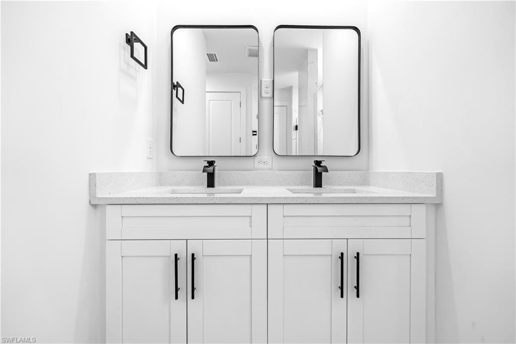 Double vanity featuring white shaker cabinetry, an integrated white countertop with speckle detailing, two undermount sinks, and matte black waterfall faucets
