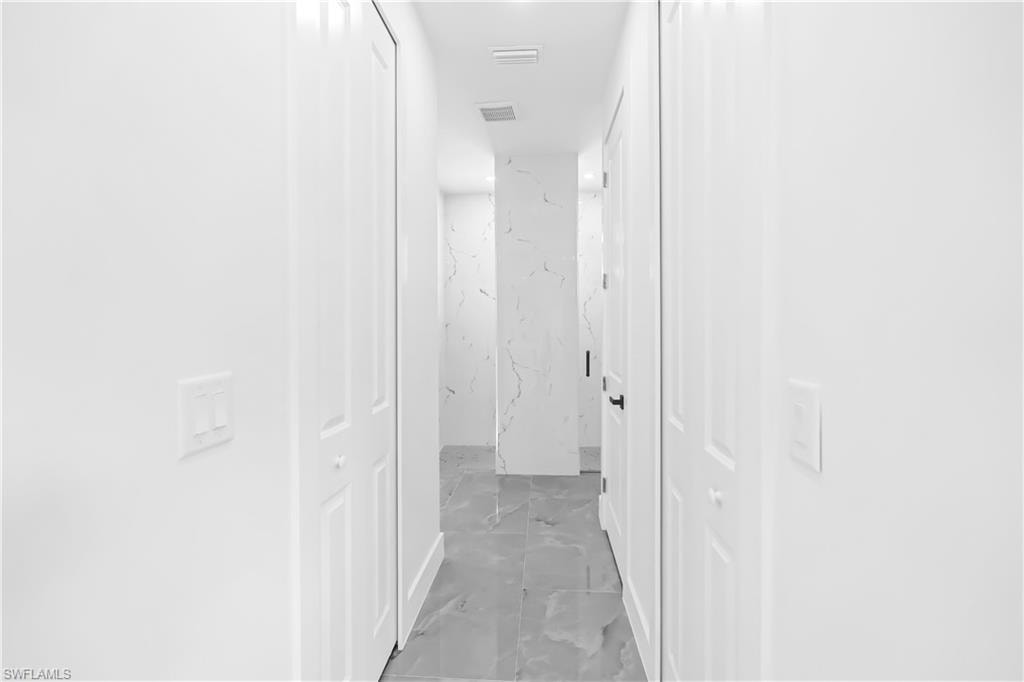 Hallway featuring light gray tile flooring, crisp white walls, white bifold doors, and a decorative wall panel with a subtle veined pattern