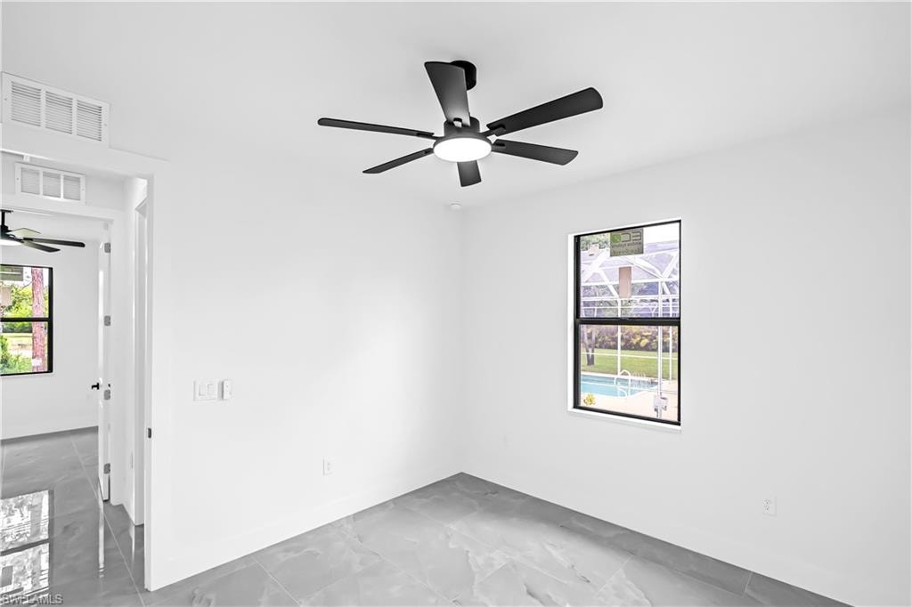 Bright interior space featuring a matte black ceiling fan with integrated lighting, large format tile flooring, and a window overlooking a screened pool area