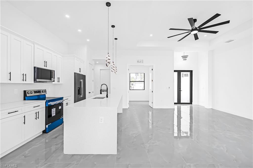 Contemporary kitchen featuring a large island with a sink, white shaker cabinetry with black hardware, and stainless steel appliances