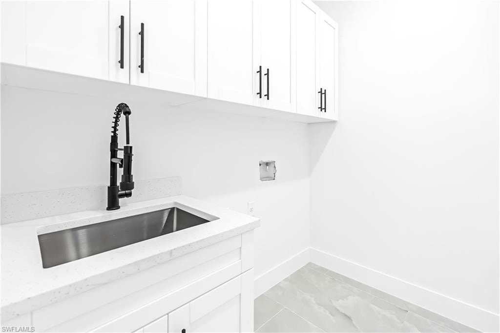 Utility sink with a matte black pull-down faucet, white upper and lower cabinetry with black hardware, white solid surface countertop, and light gray tile flooring