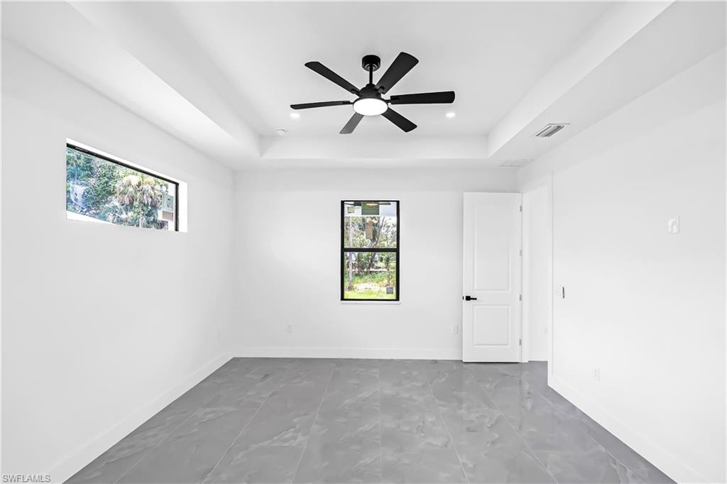Spacious room featuring modern gray tile flooring, a contemporary black ceiling fan with integrated lighting, and a tray ceiling