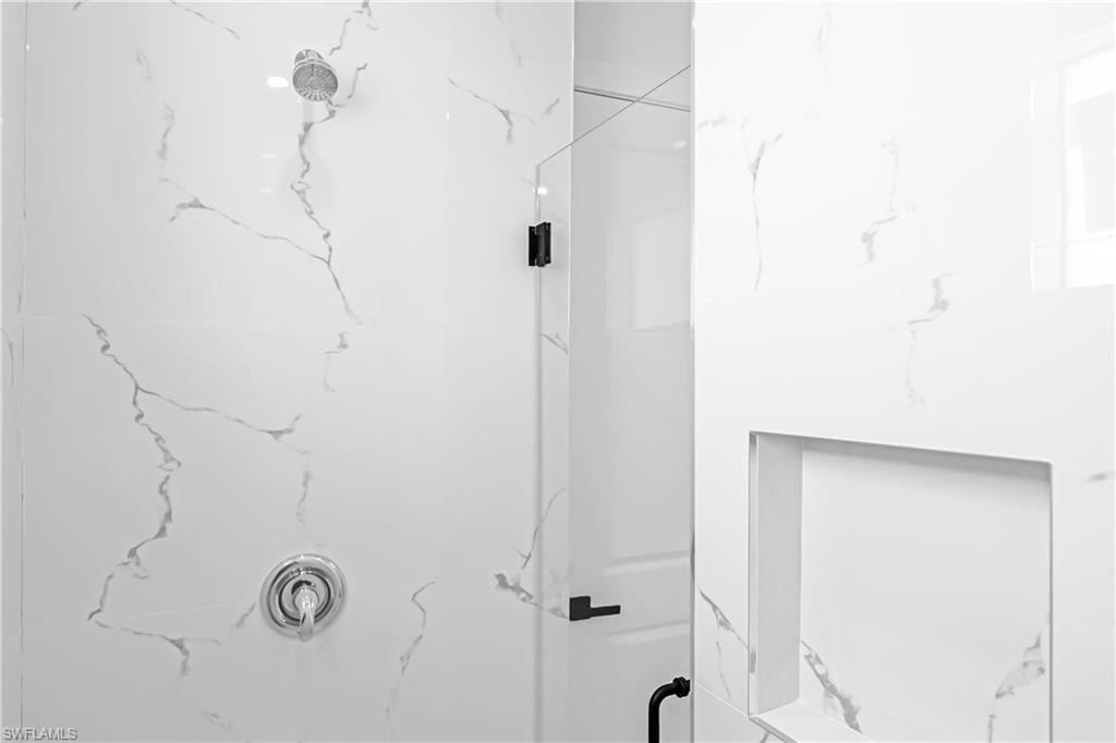 Shower with large format white tile featuring gray veining, a built-in niche, and a glass enclosure with matte black hardware