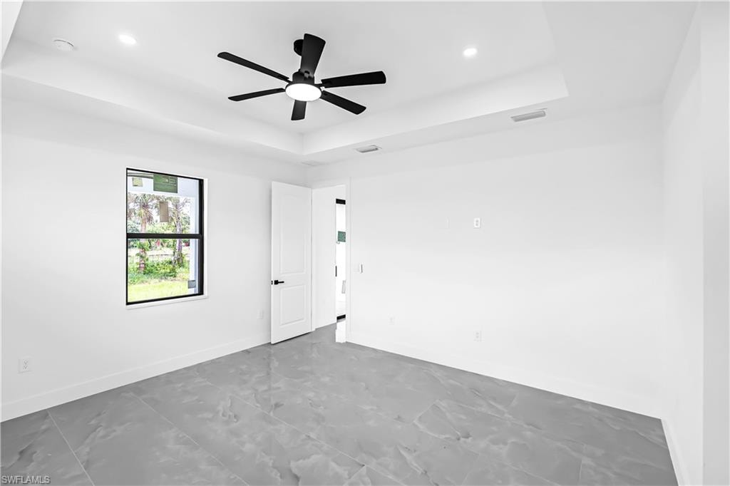 Spacious room featuring large format tile flooring, a tray ceiling with a modern ceiling fan, recessed lighting, and a single window with black trim