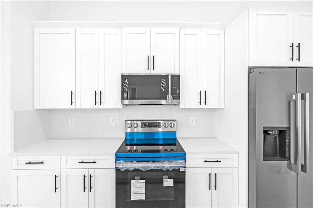 Contemporary kitchen featuring white shaker cabinetry, stainless steel appliances, speckled white countertops, and a matching backsplash