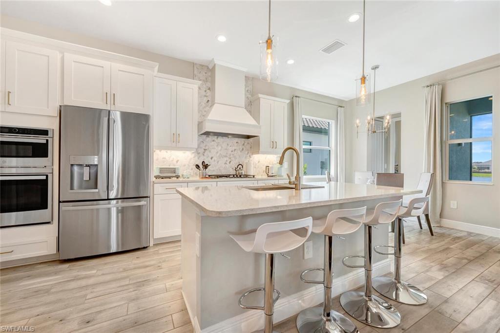 Kitchen with light hardwood / wood-style flooring, tasteful backsplash, custom exhaust hood, stainless steel appliances, and pendant lighting