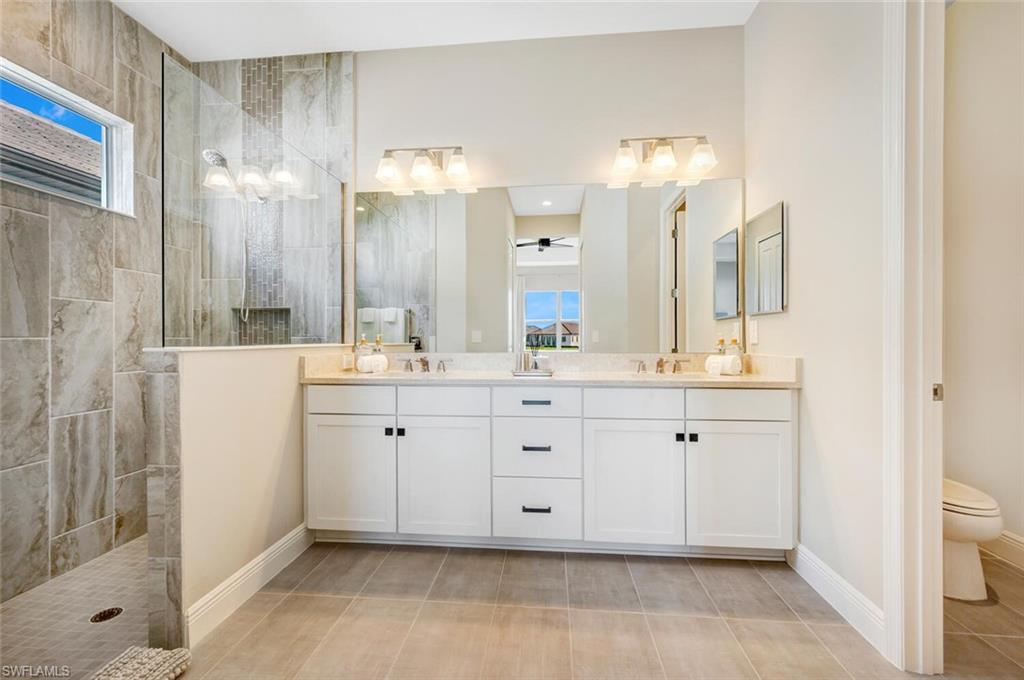 Bathroom with tiled shower, dual sinks, toilet, tile flooring, and large vanity