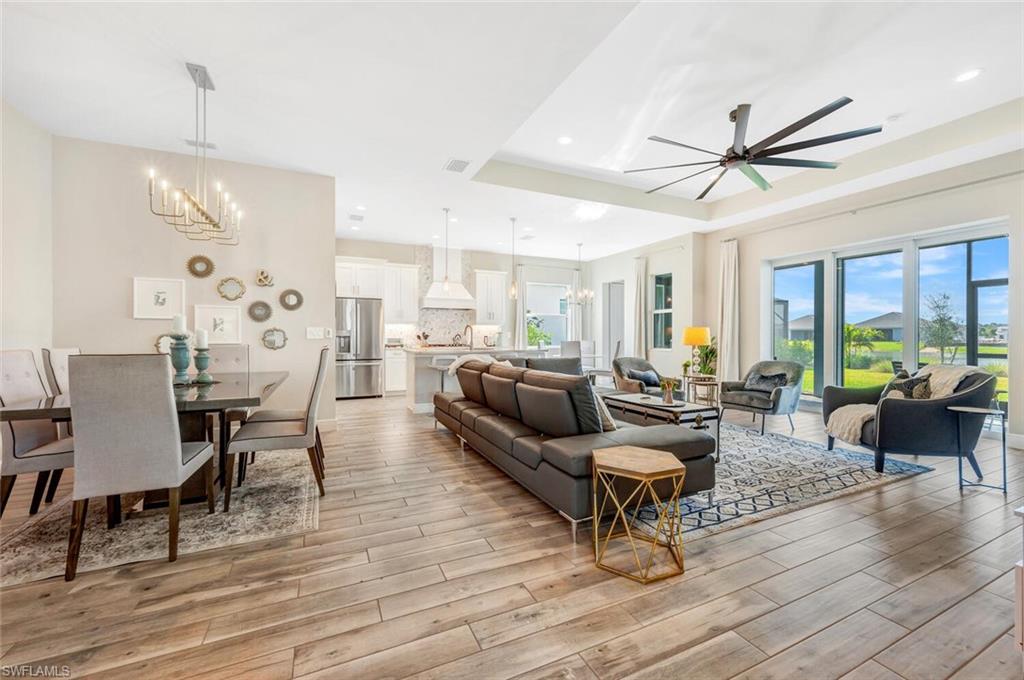 Living room with ceiling fan with notable chandelier, a tray ceiling, light wood-type flooring, and a healthy amount of sunlight