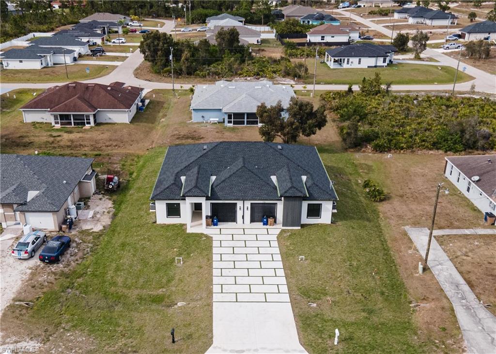 Modern duplex featuring a dark shingle roof, white exterior walls, and a distinctive patterned concrete driveway